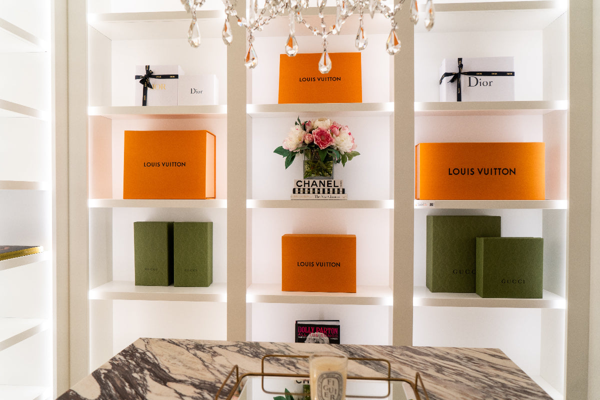 Bright and light closet lit up with LED lighting on the edges showing orange Louis Vuitton boxes, Chanel, and flowers