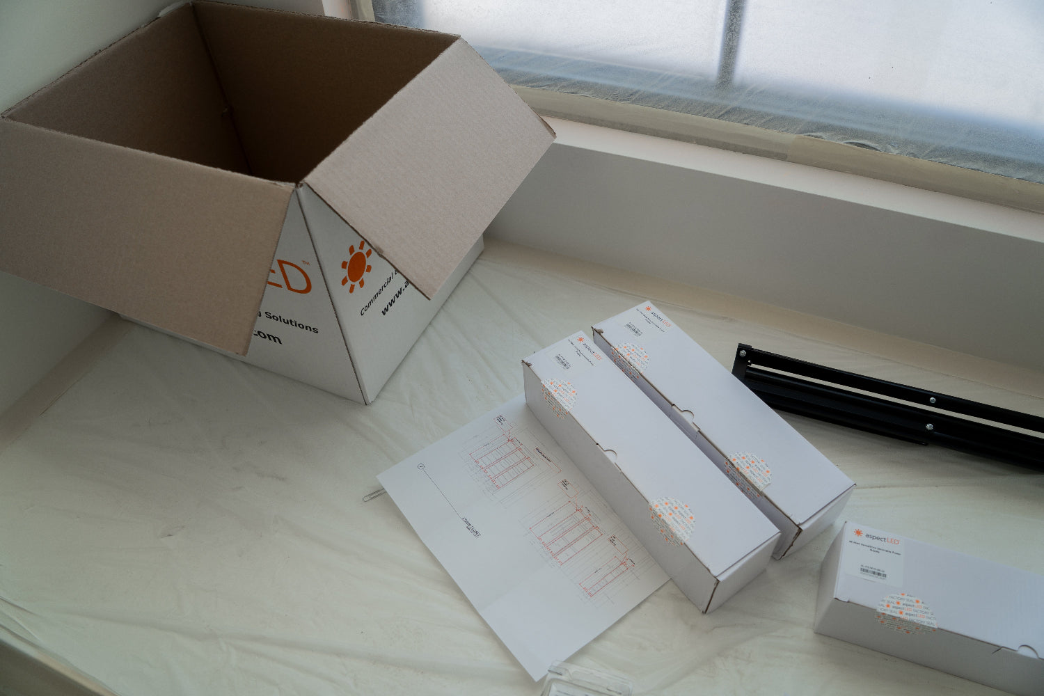 aspectLED opened box next to products in boxes with plans underneath the boxes