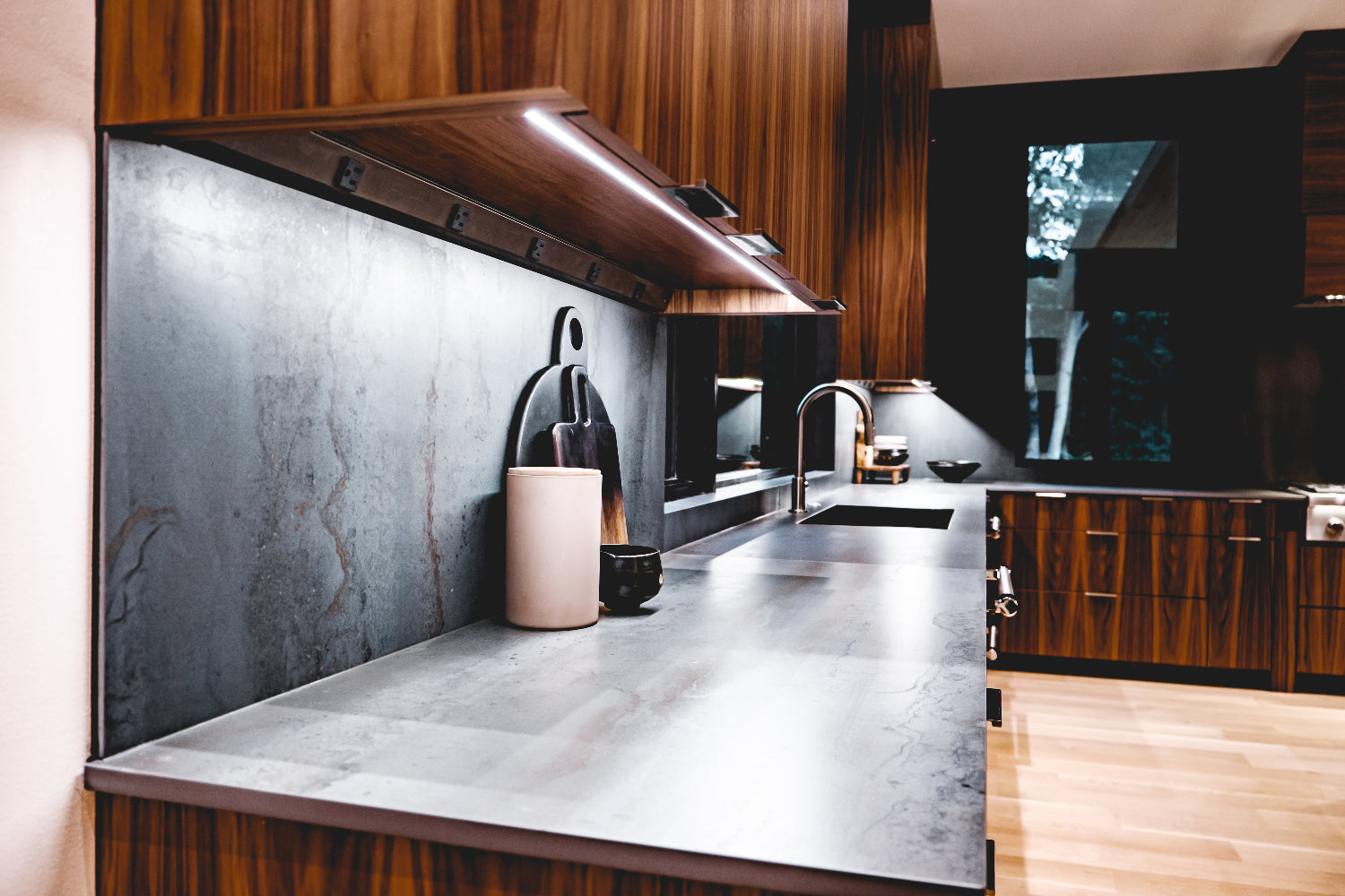 Modern kitchen with stainless steel countertop, wooden cabinets, and a television screen.