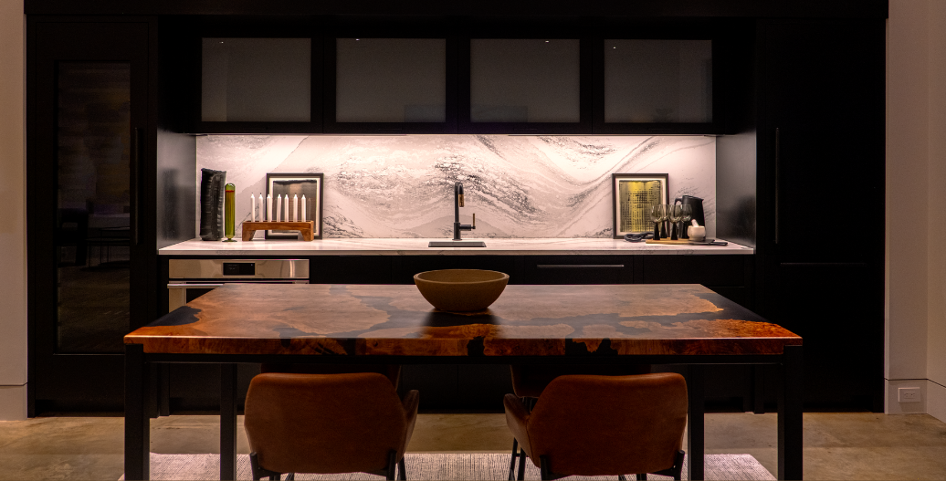 Modern kitchen with black cabinets and warm LED under cabinet lighting illuminating the countertop and backsplash.