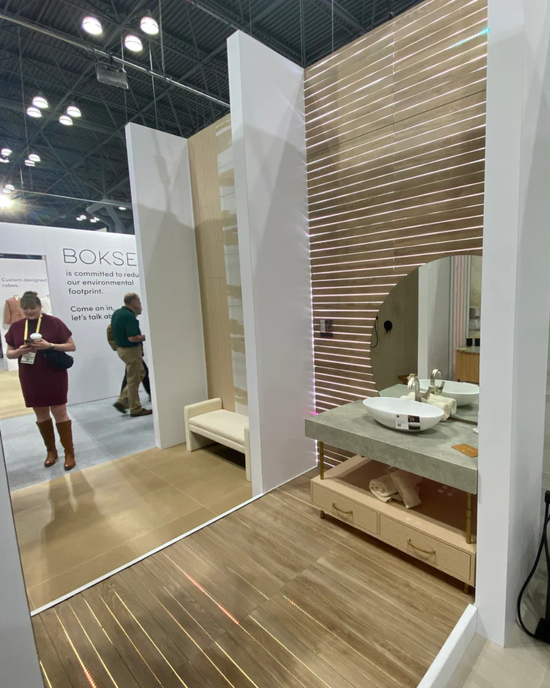 Bathroom setup with wooden floor and white walls at an exhibition, featuring a sink and mirror.