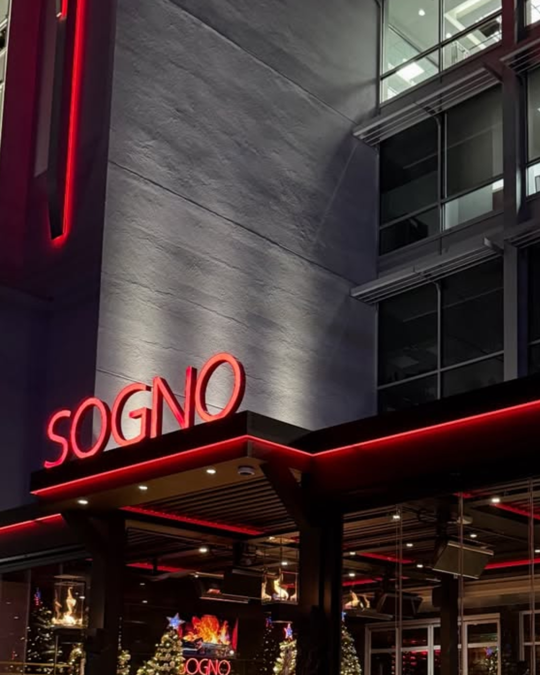 Neon sign 'Sogno' on a building exterior at night being lit up by strip lights