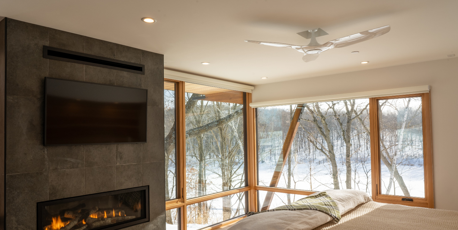 Modern bedroom with fireplace, TV, and large windows overlooking a snowy landscape.