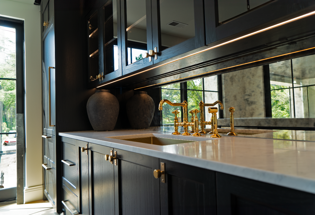 Modern kitchen with dark cabinets, gold fixtures, and a large mirror.
