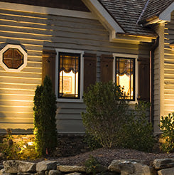 Cottage exterior with warm lighting, stone wall, and trees.