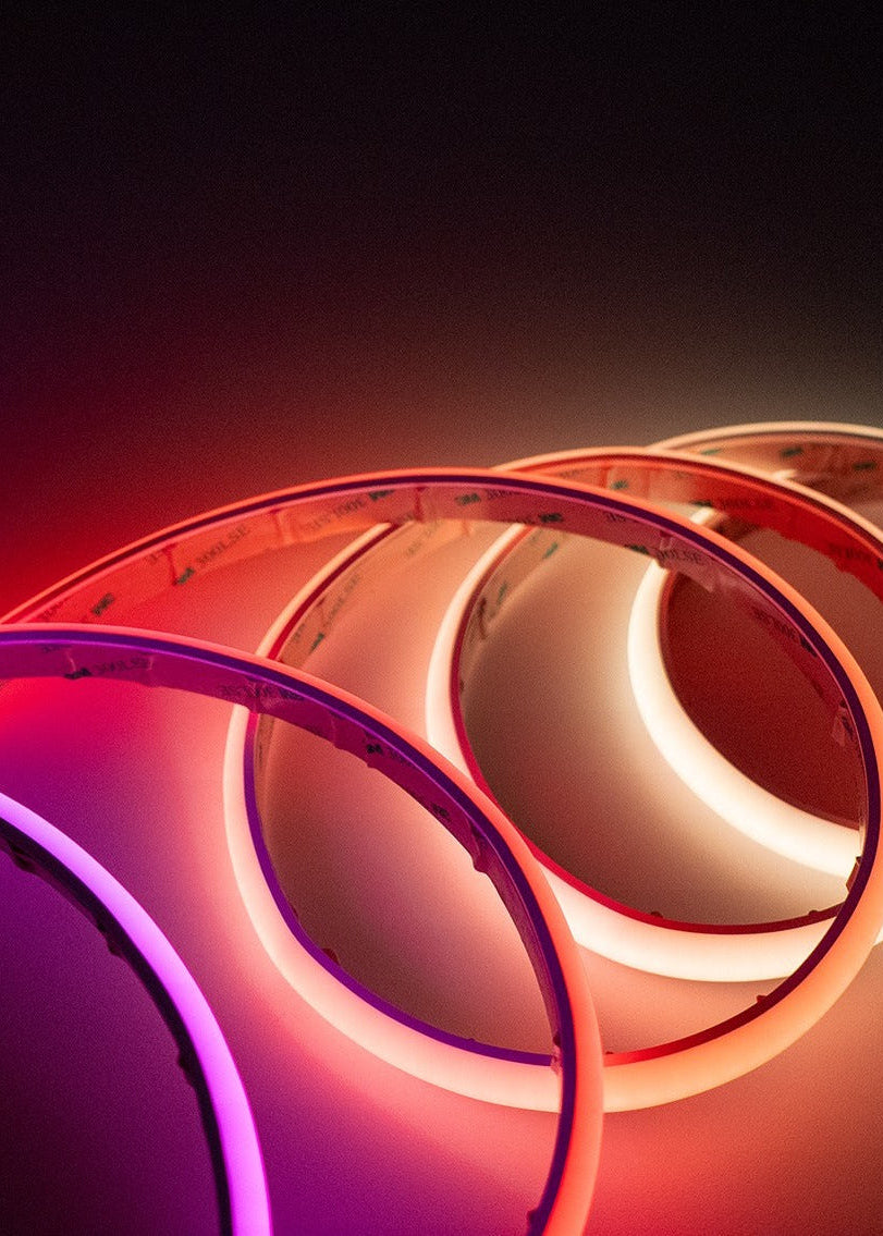 A close-up of overlapping circular LED light strips glowing in pink, purple, orange, and white against a dark background.